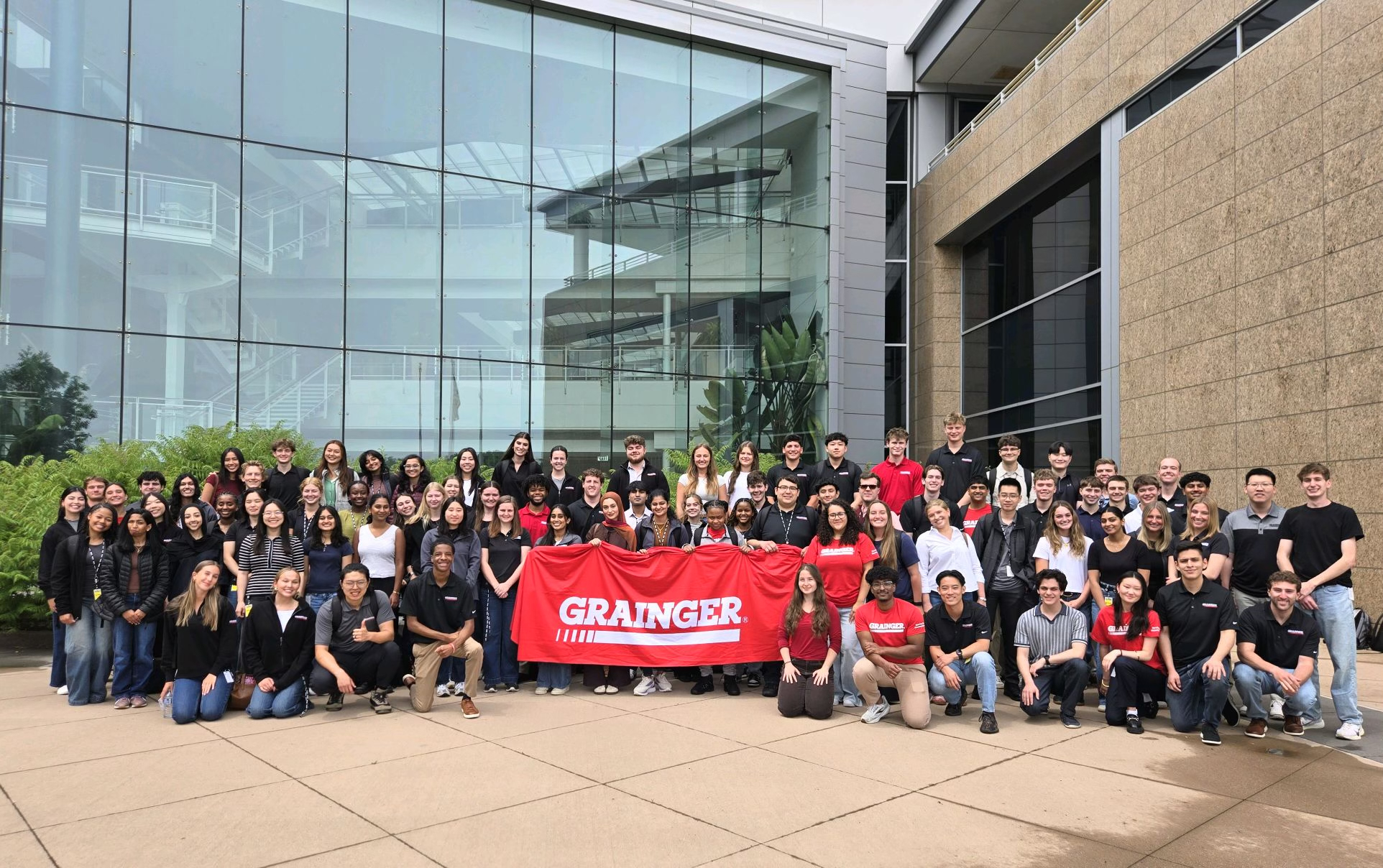 Group photo of the Grainger team gathered outdoors holding a red Grainger banner.