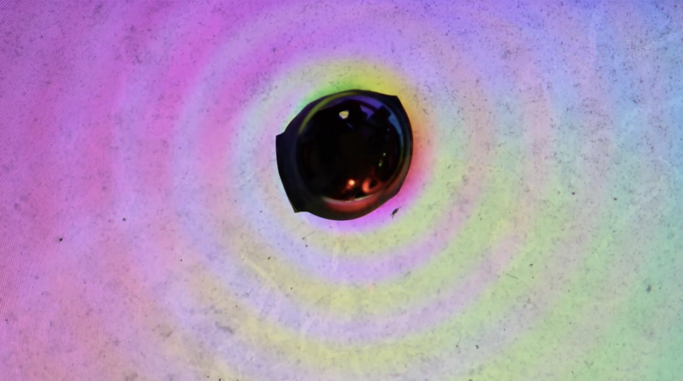 Controlled wave generator creating concentric surface waves over a colored illumination pattern.